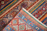 Folded edge of Khorjin rug, displaying geometric diamond motifs, vibrant striped bands, and fringe.