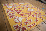 Angled detail of raised raspberry red floral patterns on a saffron yellow flatweave mat.