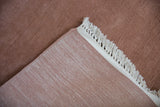 Plush dusty rose pile, woven foundation, and white fringe on a vintage carpet.
