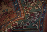 Geometric green, madder red, and ivory patterns on a folded vintage Indian Lotto Soumac rug.