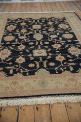 Serrated pink florals on charcoal field, antique ivory border, and fringe of Soumac rug.
