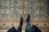 Dusty blue vintage Indian Shirvan rug with Perpedil motifs and starburst florals, seen with boots.