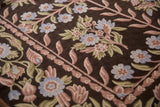 Intricate curvilinear chainstitch floral detail in dusty mauve, blue, and green on dark brown.