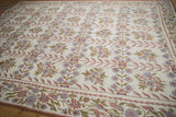 Vintage chainstitch carpet detail: intricate curvilinear floral border with dusty rose vines and faded blue blooms.