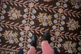 Dark brown vintage chainstitch rug with dusty floral vines under black boots.