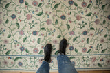 Ivory chainstitch rug with curvilinear floral vines, subtle spiraling texture, green, lavender, red.