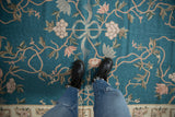 Arts and Crafts style curvilinear floral pattern on turquoise chainstitch carpet with a light border.