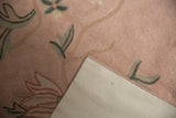 Chainstitch rug corner with rose spiraling texture and green florals, showing cotton canvas backing.