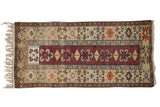 Vintage Melas rug runner with a central column of geometric motifs in copper, rust, and sand tones.