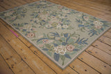 Vintage chainstitch rug corner displaying curvilinear floral sprays in blue, pink, and sage green.