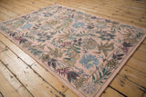 Detailed curvilinear floral border and vine motifs on a pink vintage chainstitch rug.