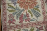 Vintage chainstitch carpet detail featuring curvilinear floral motifs and a winding mauve border.