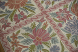 Chainstitch curvilinear floral design detail in pink, olive, and slate blue on ivory.