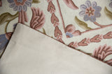 Vintage chainstitch rug showing blush floral vines and light canvas backing.