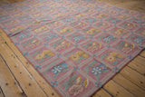 Curvilinear dusty mauve chainstitch rug with sky blue and saffron yellow floral sprays.