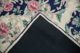 Chainstitch carpet corner revealing black canvas backing and curvilinear floral design.