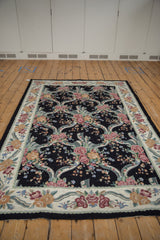 Close-up of vintage chainstitch carpet, showing blush floral sprays on black field with ribbon trellis.