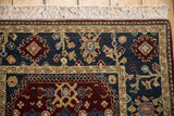 Corner view of the hand-knotted rug's palmette border, pawn motif, and intact white fringe.