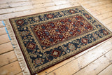 Vintage Armenian rug with a burgundy field and teal border, shown from a high angle.