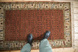 A person stands on a vintage Armenian rug, showing the scale of its rust-colored field and geometric border.