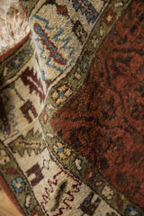 A close-up of the plush, hand-knotted wool pile and serrated leaf border in rust and dusty blue.