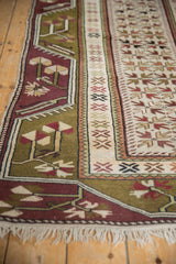 Close view of the vintage Melas rug's border, showing geometric florals in moss green and plum.