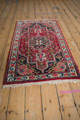 Vintage Persian Bijar rug with a bold geometric medallion and ruby red field shown from an angle.