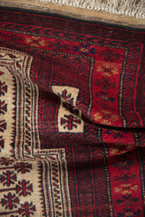 Close-up of folded vintage Belouch rug, showing cherry red and beige snowflake and arrowed patterns.