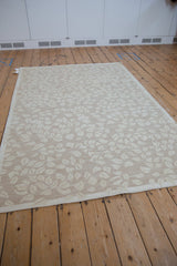 Ivory leaves in a dancing spiral pattern with a simplistic border on a pale sand Indian Soumac carpet.