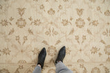 Pale coffee brown Rococo floral arabesques on ivory Indian Soumac carpet, feet visible.