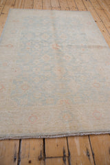 Angled view of Peshawar rug's allover floral pattern, pale ivory with blue and terracotta accents.