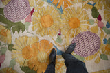 Plush Art Deco rug detail: yellow serrated flowers, aubergine checker motif, green leaves, feet.