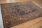 Angled view of a vintage Armenian rug's navy floral field and contrasting chestnut rust border.