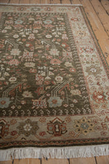 Angled view of a vintage Armenian rug with blossom and boteh motifs on its deep sage green field.