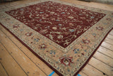 Corner view of a vintage Armenian rug with a sand floral border and a wine-red field of scrolling vinery.