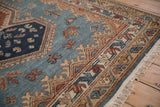 Corner view of a vintage rug's intricate vine border and full pile beside the fringe.