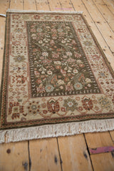 Angled view of a vintage Armenian rug showing its plush olive pile and ivory floral border.