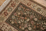 Corner of a vintage Armenian rug showing plush olive pile, floral ivory border, and cotton fringe.