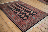 Angled perspective of a vintage Bokhara rug highlighting the sheen on its plush, dark pile.