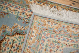 Folded vintage Indian Kerman rug with floral pile, ivory fringe, and original side selvage.