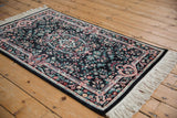 Close-up of vintage Pakistani Savonnerie rug corner, black field, ivory border, and floral patterns.
