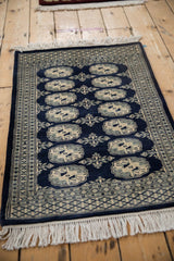 Corner of vintage Bokhara rug with ivory fringe and cobalt blue geometric borders.