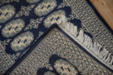 Folded vintage Bokhara rug corner, showing white fringe and geometric gul motifs.
