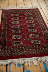 Cherry red vintage Bokhara rug's geometric gul motifs, multi minor borders, and white fringe.