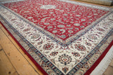 Pakistani Isfahan design rug corner featuring cherry red floral field and ivory arabesque border.