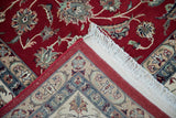 Isfahan design rug corner: cherry red field, beige floral border, white fringe.