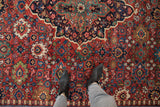 Floral palmettes and vinery in blue and green on the abrashed rust-red field of a vintage Mahal carpet.