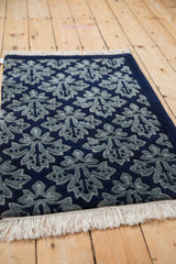 Angled perspective on the plush pile and raised damask leaf pattern of a vintage blue rug.