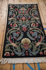 Savonnerie rug close-up: looped pile floral blossoms, scrolled vines in blush, green, blue, and sand.