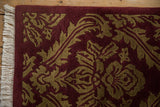 The carved, damask-inspired beige leaf pattern on a burgundy pile, with intact ivory fringe.